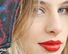 a close up of a person with a red lipstick and piercing on her nose, wearing a bandana