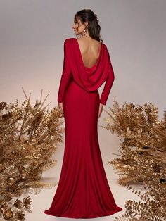 a woman in a long red dress is standing next to some plants and gold leaves