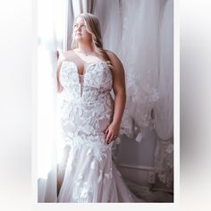 a woman standing in front of a window wearing a wedding dress