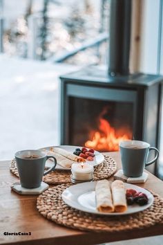 two cups of coffee are sitting on a table next to a fire place with pastries in front of it