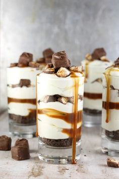 four desserts with chocolate and marshmallow toppings in glass cups on a table