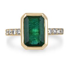 an emerald and diamond ring in yellow gold with diamonds on the band, set against a white background