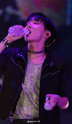 a male in a black jacket and silver shirt is drinking from a water bottle while standing on stage