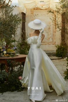 a woman in a white dress and hat is standing near a table with flowers on it