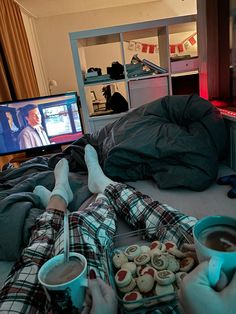 two people laying on a bed with their feet up in the air while watching tv