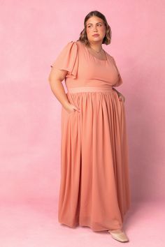 a woman standing in front of a pink background wearing a dress with ruffle sleeves