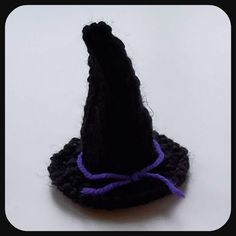 a black crocheted witches hat with purple thread on the top and bottom, sitting on a white surface