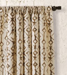 the curtain is hanging in front of a white brick wall with brown and tan designs on it