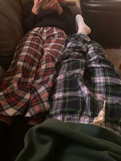 a man laying on top of a couch next to a woman in plaid pajamas and holding a cell phone