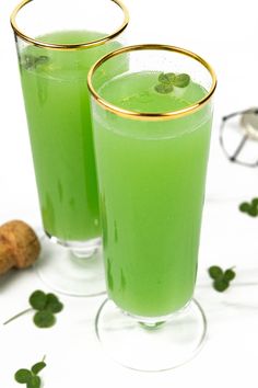 two glasses filled with green liquid sitting next to each other