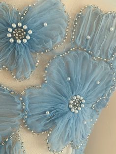 three blue flowers with pearls and beads on the petals are attached to a piece of fabric