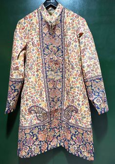 Step into elegance with our Woven Wool Kani Jamawar Coat, adorned with an intricate paisley floral pattern on both the front and back. This soft and lightweight trench coat is an ideal choice for spring and cool summer days, providing both style and comfort. Crafted from the renowned Kashmiri Kani shawl, woven with traditional techniques in Kashmir, this coat is a beautiful and timeless piece. The same Kani Shawl fabric is expertly tailored into this coat, ensuring a seamless blend of heritage and contemporary fashion. The coat's interior is lined with soft, silky, color-coordinated fabric, featuring convenient side pockets and a discreet hook enclosure on the front. With a vibrant play of colors, this jacket is a graceful addition to any occasion, effortlessly enhancing your casual and tr Traditional Silk Outerwear For Fall, Long Floral Print Winter Outerwear, Bohemian Outerwear With Paisley Print For Spring, Traditional Silk Outerwear For Spring, Bohemian Spring Outerwear With Paisley Print, Traditional Silk Long Sleeve Outerwear, Festive Long Sleeve Outerwear With Floral Print, Festive Floral Print Long Sleeve Outerwear, Festive Long Sleeve Floral Print Outerwear