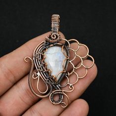 a hand holding a wire wrapped pendant with a white stone in the center and intricate filigrees around it