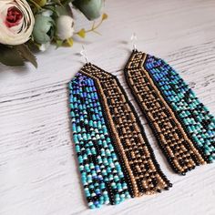 a pair of beaded earrings sitting on top of a wooden table next to flowers