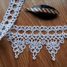 a piece of white crocheted fabric sitting on top of a wooden table next to a feather