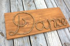 a wooden sign with the word dance written in rope on it's side, sitting on wood planks