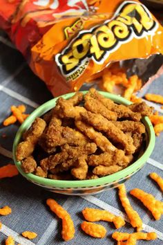 a bowl filled with cheetos sitting on top of a table next to a bag of chips