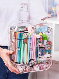 a person holding a clear container filled with pens and pencils