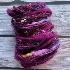 the yarn is purple and multicolored with buttons on it's end, sitting on a wooden surface