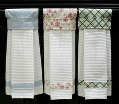 three white towels hanging from the side of a black stove top with red and green flowers on them