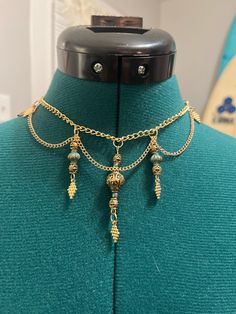 The necklace has a bohemian or vintage-inspired look, combining ornate metalwork with subtle color accents. It would add a touch of elegance to both casual and dressy outfits. Ornate Metalwork, Boho Choker Necklace, Color Accents, Boho Choker, Elegantes Outfit, Dressy Outfits, Accent Colors, Metal Working, Charm Necklace