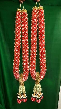 two red and white beaded necklaces hanging from a green cloth covered wall,