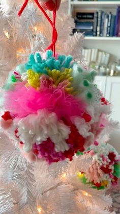 an ornament hanging from the top of a white christmas tree decorated with multicolored pom poms