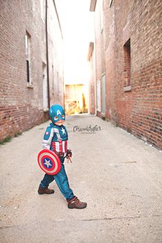 a little boy dressed as captain america walking down an alley way