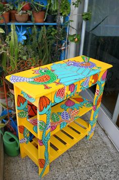 a yellow painted table sitting on top of a floor next to potted plantes