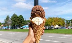 a hand holding an ice cream cone on the side of the road