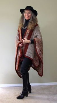 a woman in black boots and a hat wearing a ponchy shawl over her shoulders