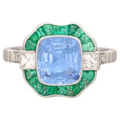 Once in a while we come upon a ring that is truly extraordinary. This is one of those cases. This showstopper features at its center a 2.35 carat unheated vibrant blue cushion cut sapphire set in a gorgeous design surrounded by a halo of stunning emeralds and flanked by 8 old cut diamonds for approximately 0.43 carats total. The antique platinum ring is in phenomenal condition, is a size 6.75 (easily resized up or down as needed) and weighs 5.8 grams. The gorgeous unheated cornflower blue sapphire is accompanied by GIA report #2225824739 confirming the stone is indeed unheated and showing its geographic origin as Sri Lanka. The perfect alternative engagement ring or cocktail ring for someone looking to separate themselves from the crowd! Platinum Emerald Ring, Sapphire Cocktail Ring, Emerald And Diamond Ring, Colored Stone Rings, Vintage Cocktail Ring, Platinum Diamond Rings, Emerald Diamond Ring, Blue Sapphire Diamond, Diamond Cocktail Rings