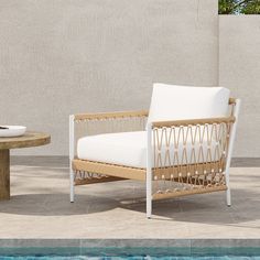 a white chair sitting next to a pool with a wooden table in front of it