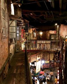 several people are sitting at tables in an old warehouse like area with stairs and railings