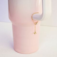 a pink coffee mug with a gold initial charm on the handle and a chain attached to it