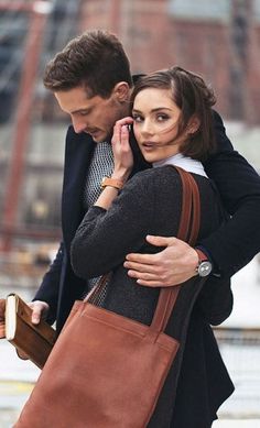 a man and woman walking down the street while talking on their cell phones, one holding a brown bag