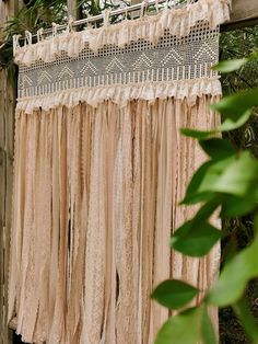 an old fashioned curtain hanging from a wooden fence in front of some green plants and trees