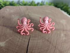 two pink octopus shaped earrings sitting on top of a wooden table next to green plants