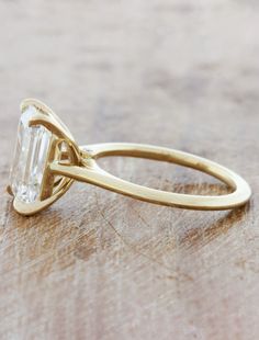 a yellow gold ring with an emerald stone in the center on a wooden table top