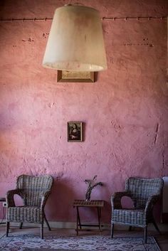 two wicker chairs and a lamp in a room with pink paint on the walls