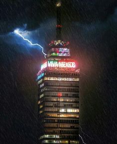 a very tall building with a lot of lights on it's side in the rain