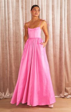 a woman standing in front of a curtain wearing a pink dress