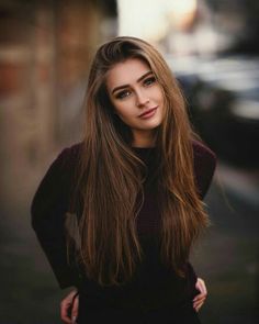 a woman with long brown hair standing in front of a building and looking at the camera