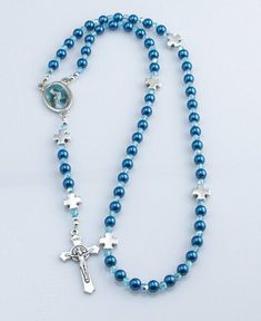 "Handmade in the USA this charming rosary was made using 6mm dark blue pearl beads with Czech fire-polished AB Aquamarine glass accent beads and features metal \"Our Father crosses, Rosa Mystica pictured on the rosary centerpiece and a Benedictine crucifix. You can customize it with a choice of five different rosary centerpieces. This affordable Catholic gift is perfect for Baptism, First Communion, Confirmation, RCIA Candidates, or for anyone who would like a lightweight rosary. It comes in a d Blue Rosary With 8mm Beads And Crucifix, Blue Rosary With 8mm Beads In Cross Shape, Blue Rosary With Round Beads For Gift, Blue Rosary Bracelet For Jewelry Making, Blue Beaded Rosary As A Gift, Blue Spiritual Rosary Bracelet With 8mm Beads, Blue Cross Jewelry With 8mm Beads, Blue Cross-shaped Jewelry With 8mm Beads, Blue Cross Rosary For Gift