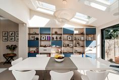 a dining room table with white chairs and a bowl of fruit on top of it