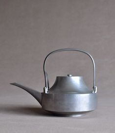 a metal tea pot with a handle on the top, sitting on a gray surface