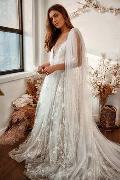 a woman standing in front of a window wearing a white gown with sheer sleeves and long veil