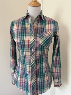 Cute 80s style madras plaid button up shirt from Mervyn's Hot Line. Made of a lightweight cotton blend. Spread collar  Patch pocket on breast. Long tail. Barrel cuffs. Yoked back. Fitted cut with darts in front and back. Probably late 70s / early 80s.  In very good used condition.  Tagged Mervyns Hot Line Size 9  55/45 cotton poly  Measurements taken flat buttoned Pit to pit 18" Waist: 16" Hips: 17" Sleeve: 30"  Length shoulder seam to hem: 26" Mervyns of California  Preppy style Madras plaid Fitted shirt  Long sleeve plaid shirt  80s style Classic Plaid Fitted Shirt, Plaid Fitted Classic Shirt, Classic Fitted Plaid Shirt, Plaid Shirt With Spread Collar And Placket, Fitted Plaid Flannel Shirt With Spread Collar, Fall Cotton Fitted Shirt, Fitted Cotton Shirt For Fall, Classic Plaid Button-up Top, Fitted Plaid Flannel Shirt With Button Closure