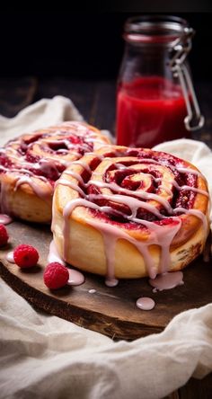 two cinnamon rolls with raspberry sauce on a cutting board