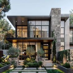 a modern house with lots of windows and plants in the front yard, as well as steps leading up to it